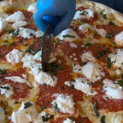 Cook cutting a pizza pie with pizza cutter